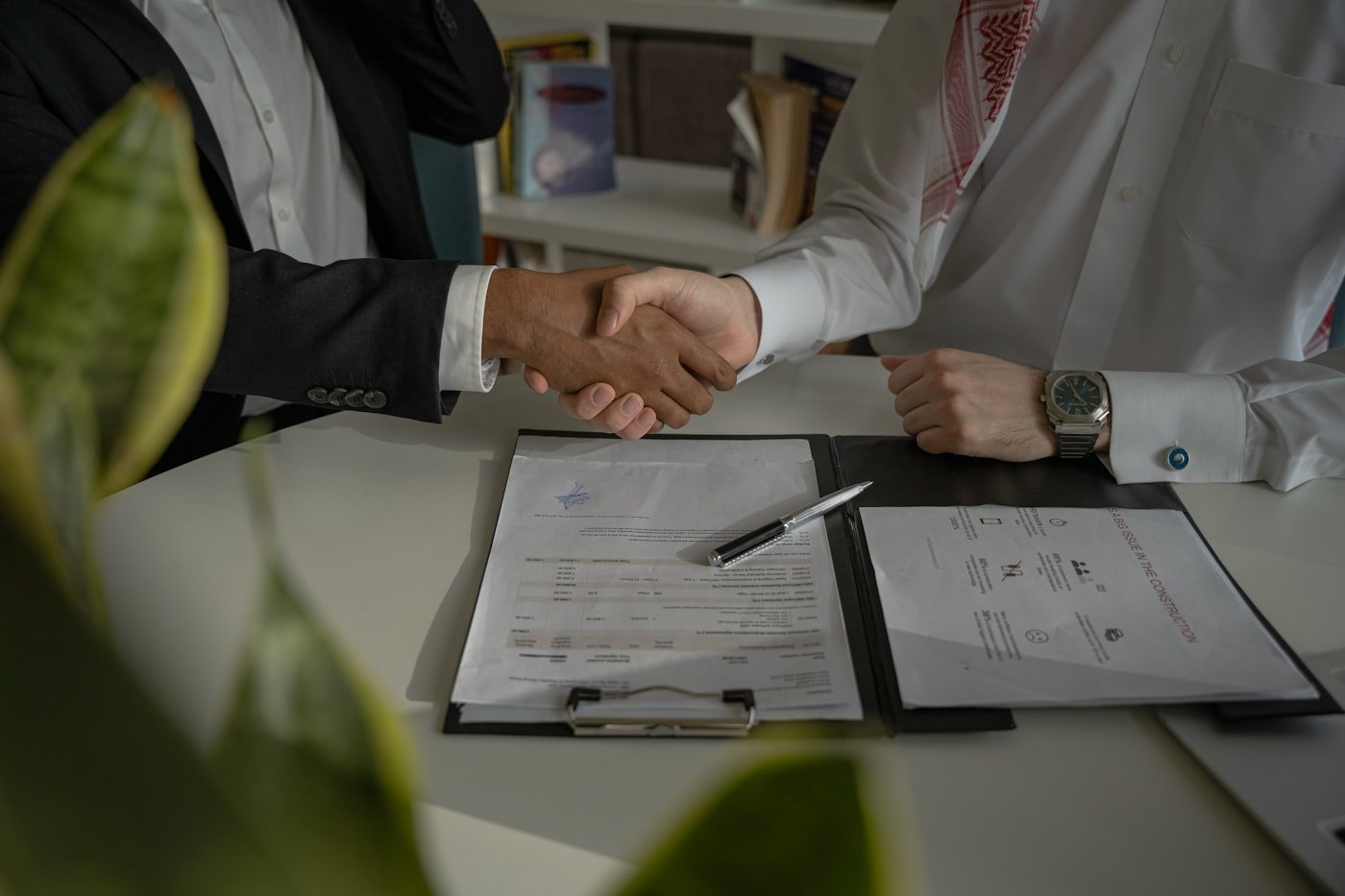 Two professionals shaking hands over signed documents